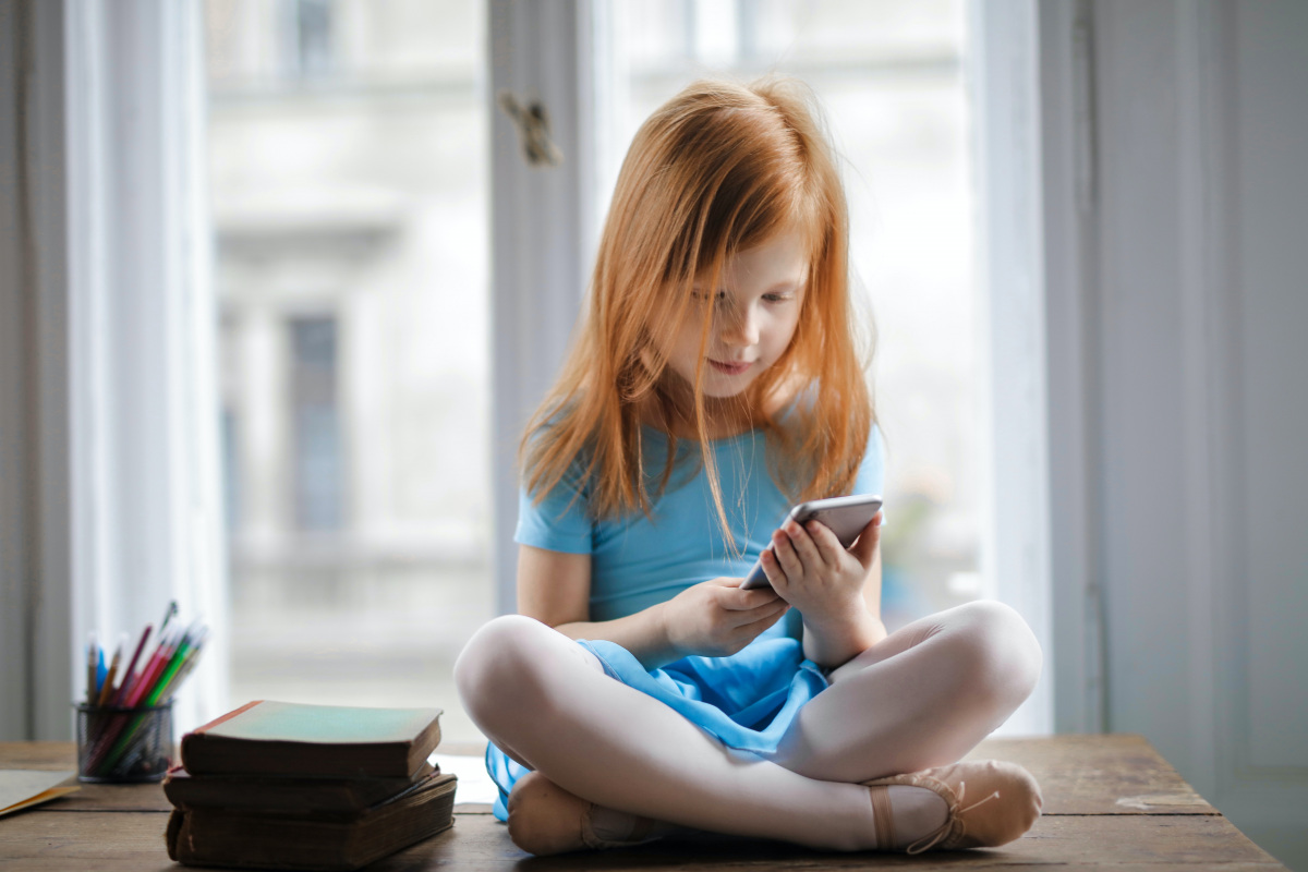 calm-small-ginger-girl-sitting-on-table-and-using-smartphone-3755620.jpg